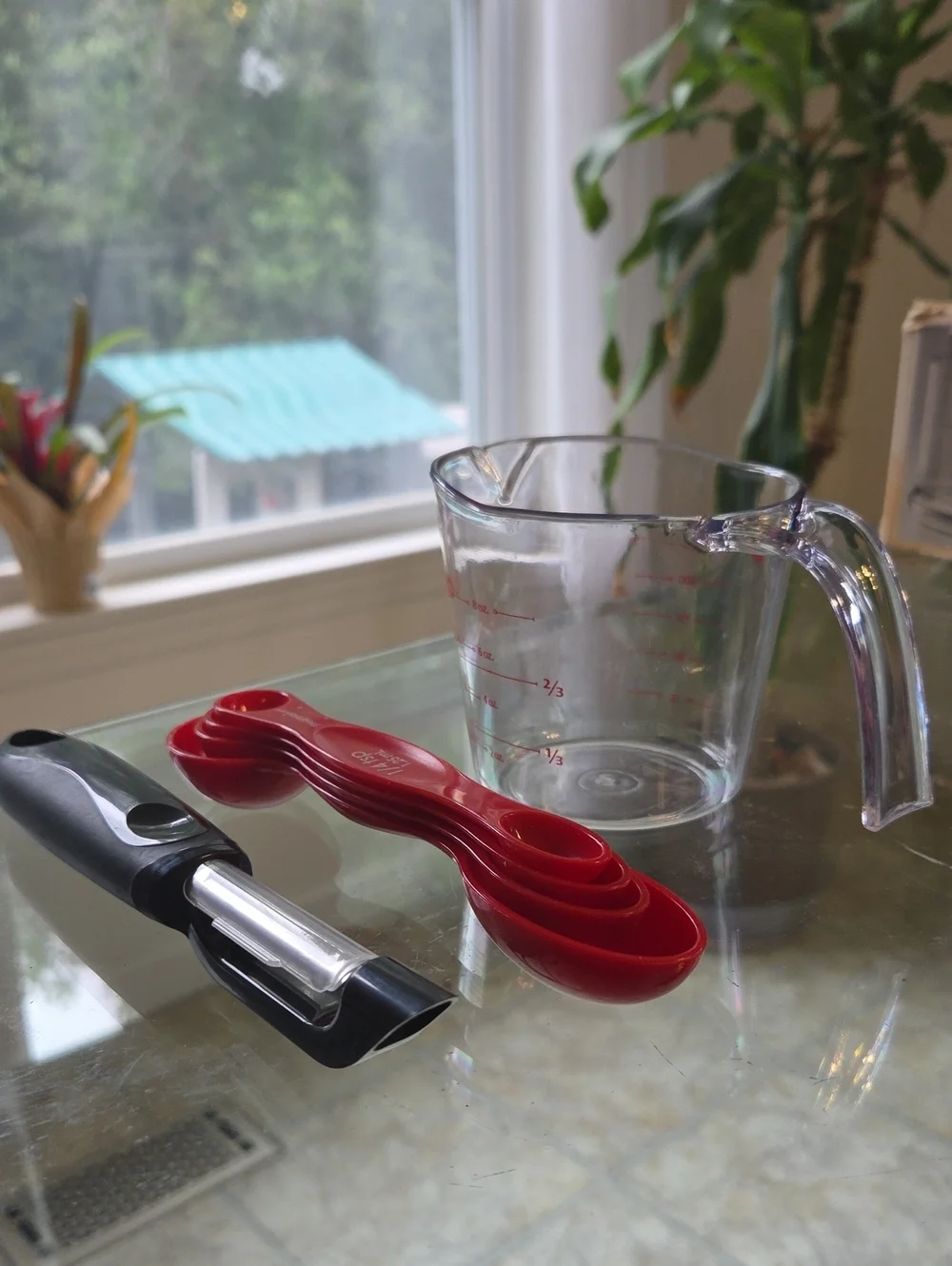 Clear Glass Measuring Pitcher with Red Nesting Measuring Spoons and Black Peeler